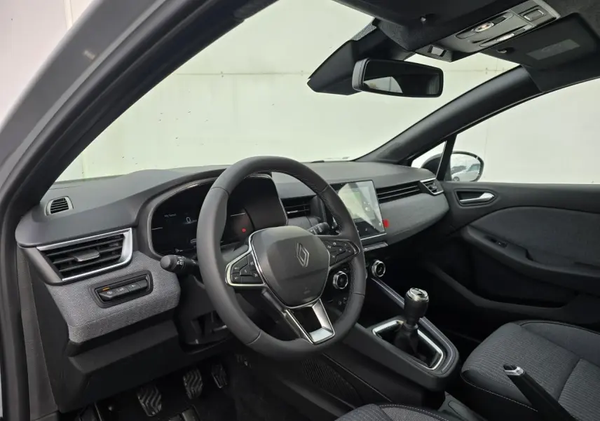 Intérieur avant droit de la Renault Clio V 2025 avec tableau de bord gris mélangé et boîte manuelle.
