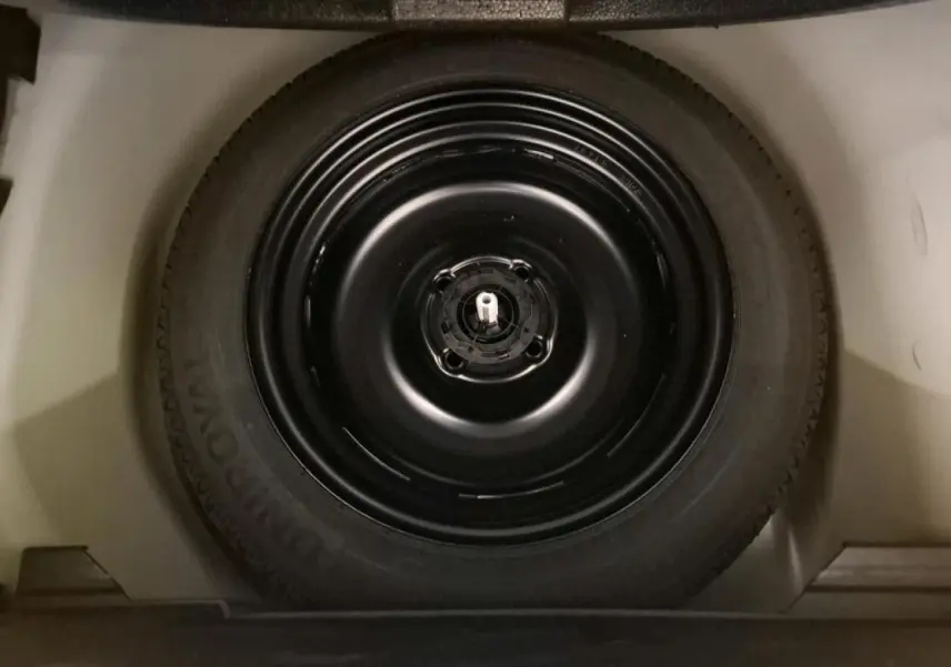 Vue rapprochée de la roue de secours noire dans le coffre d'une Peugeot 208 blanche de 2022.