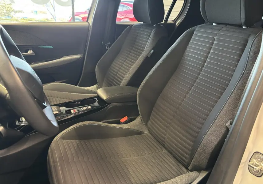 Vue intérieure côté avant droit montrant les sièges tissu gris et accoudoir central de la Peugeot 208 blanche.