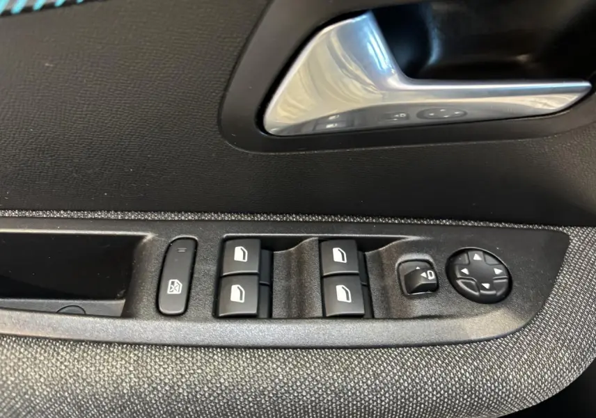 Détail des commandes de lève-vitres et réglage des rétroviseurs sur la porte intérieure côté gauche d'une Peugeot 208 blanche.