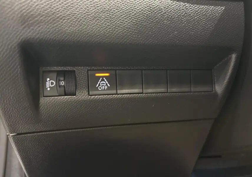 Gros plan sur les commandes noires du tableau de bord gauche d'une Peugeot 208 blanche, avec témoin d'alerte activé.
