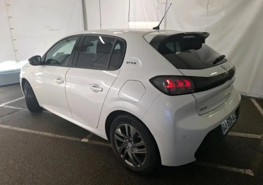 Vue 3/4 arrière droite d'une Peugeot 208 blanche avec jantes alliage et bandeau noir brillant entre feux arrière.