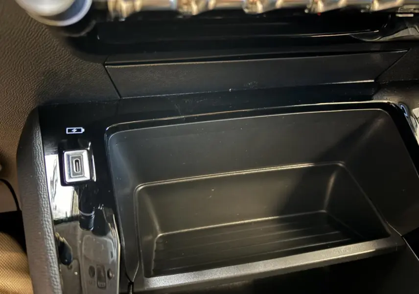 Gros plan sur la console centrale noire de la Peugeot 208 blanche, avec prise USB visible à gauche.
