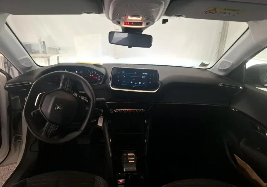 Vue intérieure avant de la Peugeot 208 blanche, montrant le tableau de bord noir avec écran tactile et volant compact cuir.