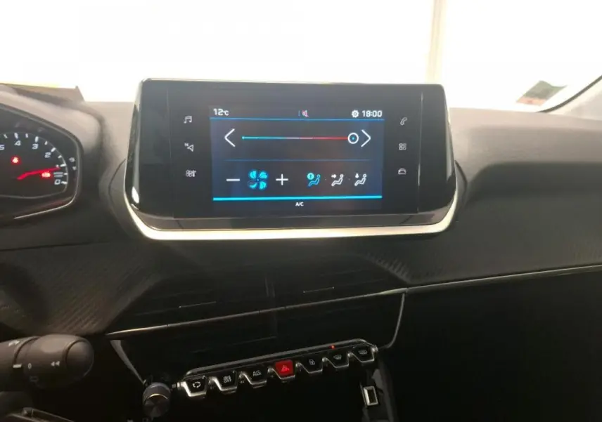 Vue rapprochée du tableau de bord de la Peugeot 208 blanche, avec écran tactile central et commandes piano noires.