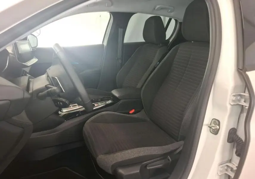 Vue intérieure côté conducteur de la Peugeot 208 blanche, sièges tissu noir avec surpiqûres bleu Azure et console centrale.