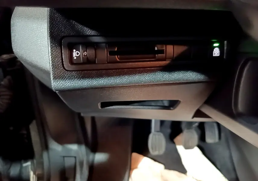 Détail intérieur du tableau de bord côté gauche avec commande de réglage des phares et pédales visibles.