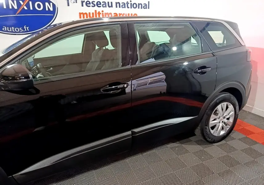 Profil côté gauche d’un Peugeot 5008 noir 2021, montrant les portes arrière et avant dans un showroom.