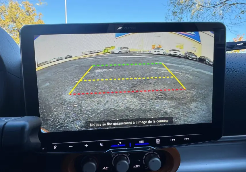 Écran de caméra de recul affichant une vue arrière avec lignes de guidage colorées, intérieur noir du tableau de bord.