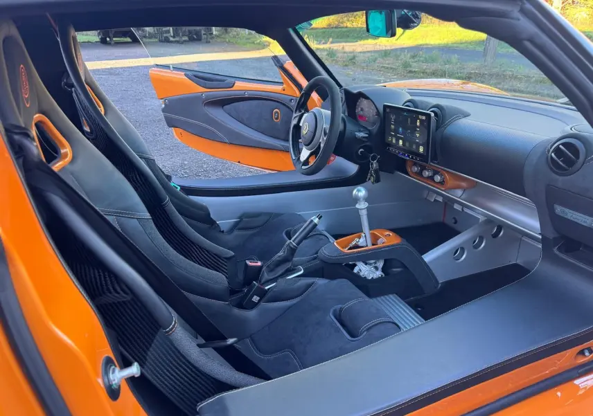 Vue intérieure côté conducteur de la Lotus Elise 3 Cup 250 orange, mettant en valeur les sièges sport en Alcantara noir et la console centrale avec levier de vitesses alu.