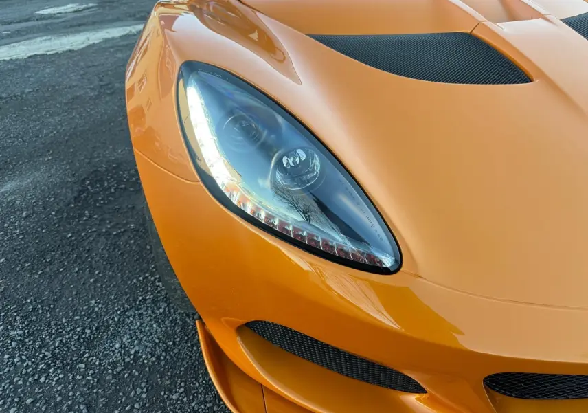 Gros plan sur l'avant gauche orange vif de la Lotus Elise 3 Cup 250 2021 avec phare halogène et prise d'air en carbone.