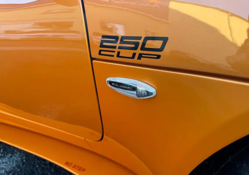 Gros plan sur l'aile avant droite orange de la Lotus Elise 3 Cup 250 avec logo "250 CUP" et répétiteur latéral.