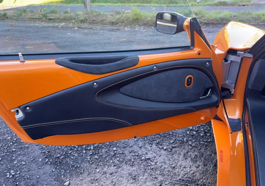 Vue rapprochée de la porte côté gauche orange de la Lotus Elise 3 Cup 250 2021 avec garniture noire et surpiqûres orange.
