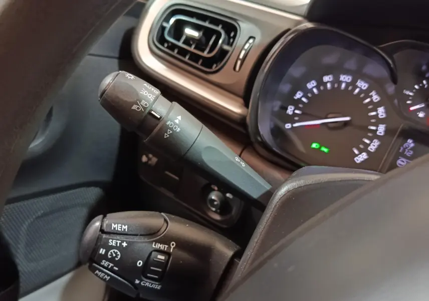 Gros plan sur le tableau de bord et commandes au volant de la Citroën C3 blanche, affichage vitesse et régulateur visible.