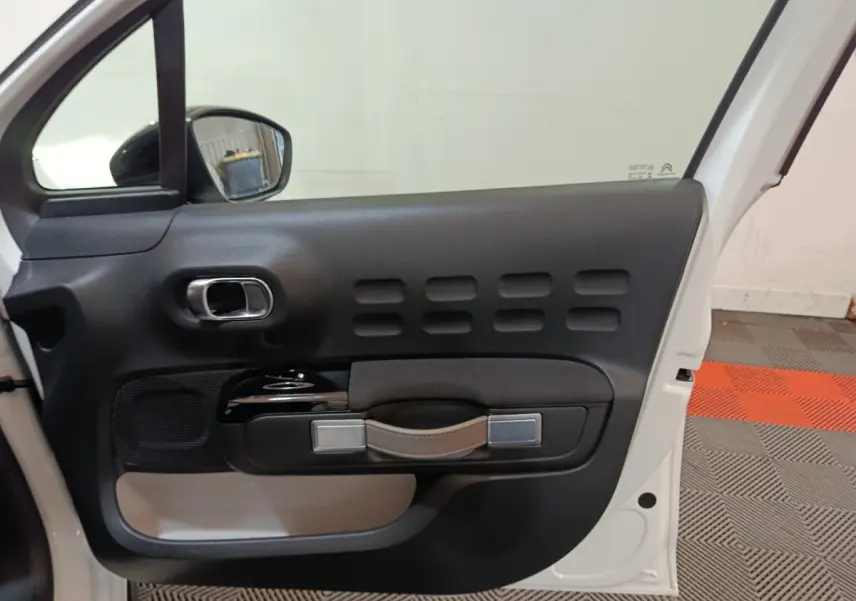 Vue intérieure de la porte avant gauche blanche de la Citroën C3 2020 avec poignée en cuir et inserts noirs.
