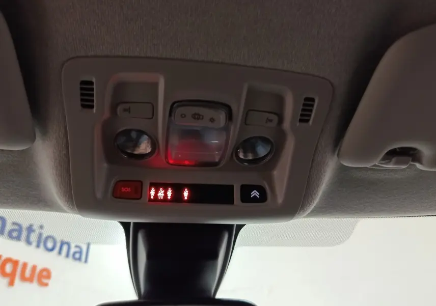 Vue intérieure du plafonnier avec commandes d’éclairage, bouton SOS et indicateurs de ceinture allumés dans une Citroën C3 blanche 2020.
