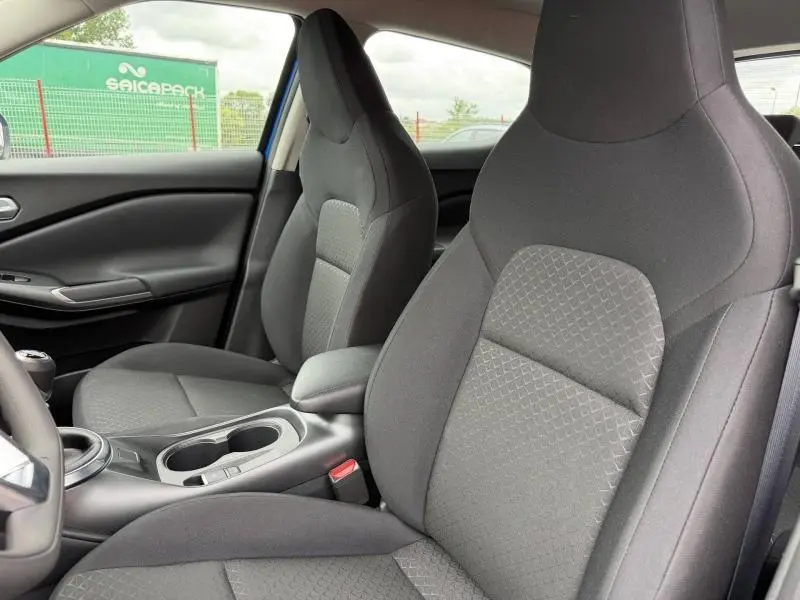 Vue intérieure côté avant droit du Nissan Juke 2025 avec sièges en tissu noir et console centrale avec porte-gobelets.