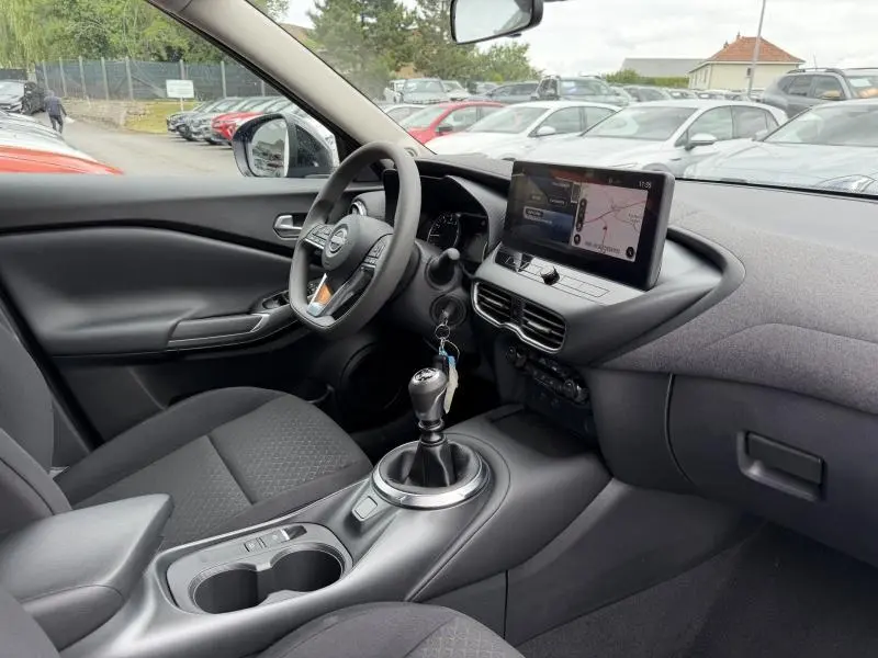 Intérieur avant droit du Nissan Juke 2025 avec tableau de bord noir, écran tactile et levier de vitesse manuel.
