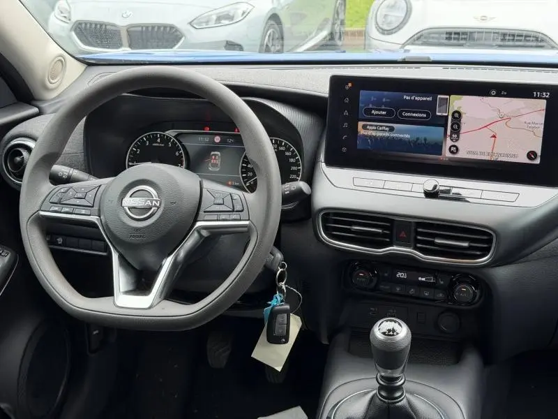 Vue intérieure du tableau de bord du Nissan Juke 2025 avec volant multifonction, écran tactile et levier de vitesses manuel.