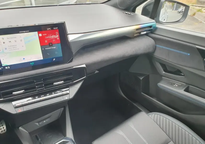 Vue intérieure côté passager de la Renault Clio VI hybride 2026, tableau de bord moderne avec écran tactile et surpiqûres bleues.