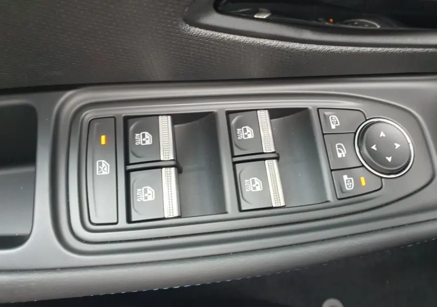 Gros plan sur les commandes de lève-vitres et réglage des rétroviseurs côté conducteur de la Renault Clio VI gris Rafale.