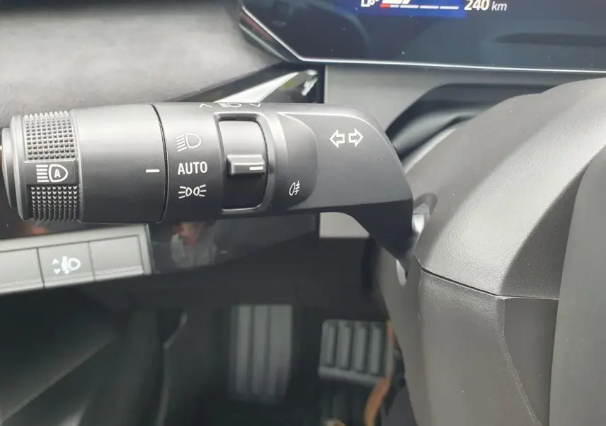 Gros plan sur la commande des feux et clignotants côté gauche du volant d’une Renault Clio VI gris Rafale, tableau de bord partiellement visible.