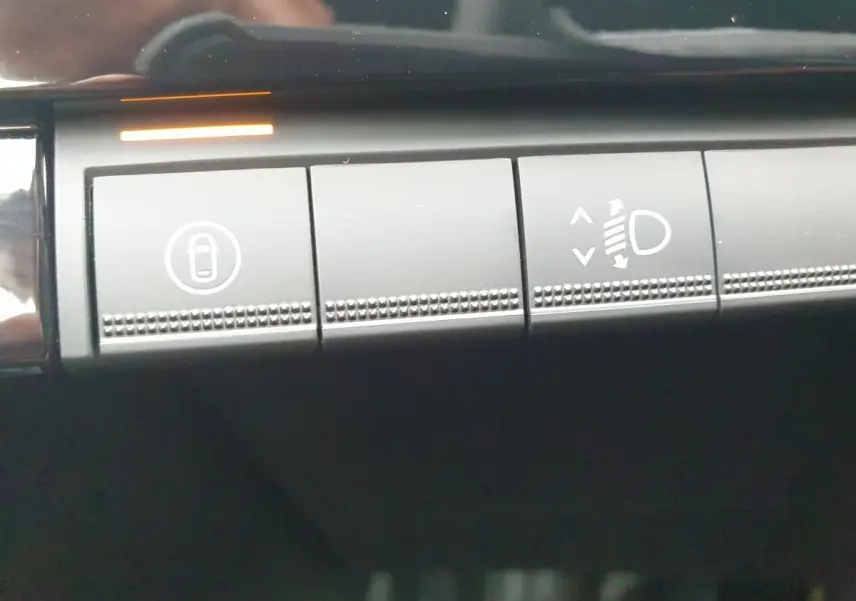 Gros plan sur les boutons de commande intérieurs gris foncé de la Renault Clio VI, avec éclairage orange actif.