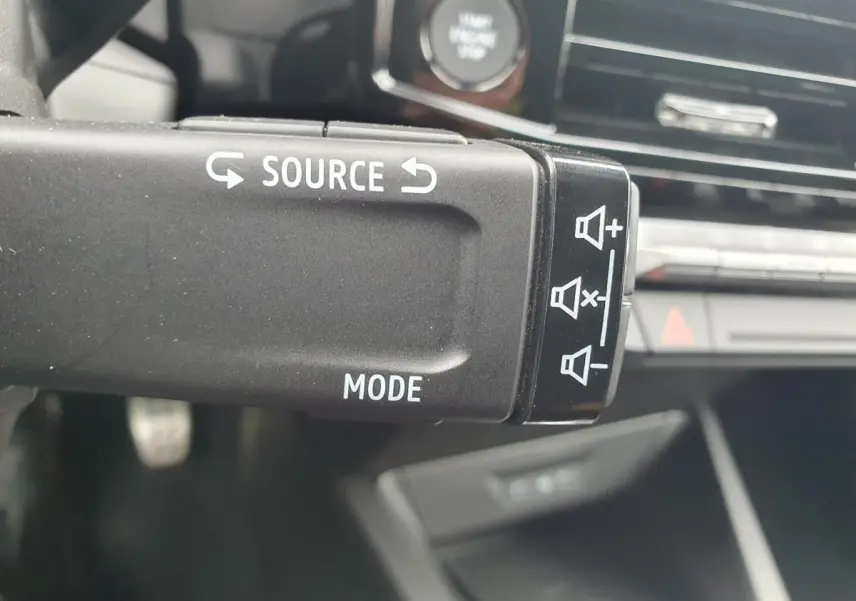 Gros plan sur la commande audio au volant de la Renault Clio VI gris Rafale, avec tableau de bord en arrière-plan flou.
