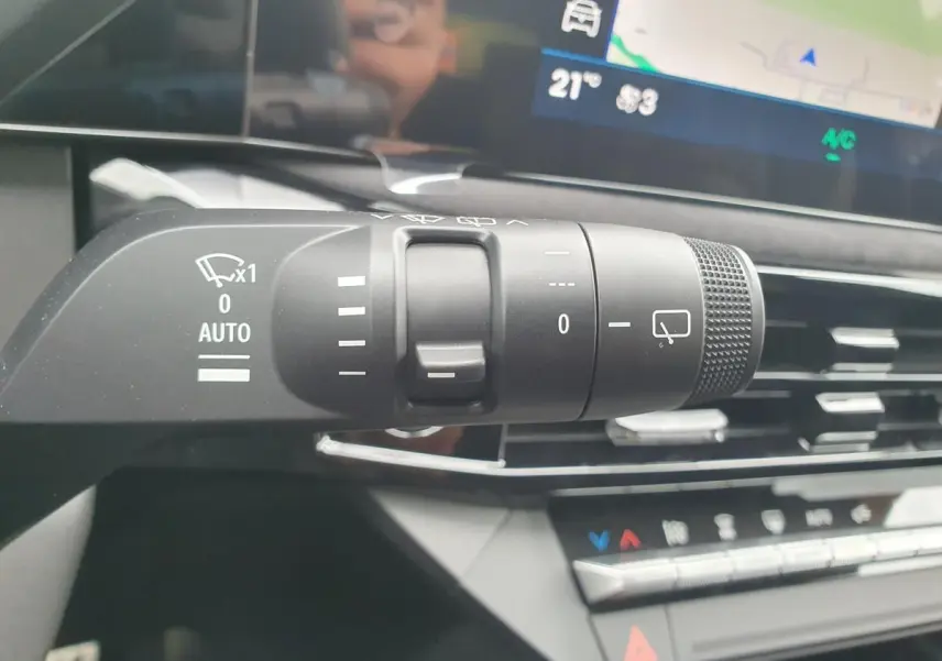 Gros plan sur la commande des essuie-glaces dans l’habitacle de la Renault Clio VI gris Rafale, avec écran tactile en arrière-plan.