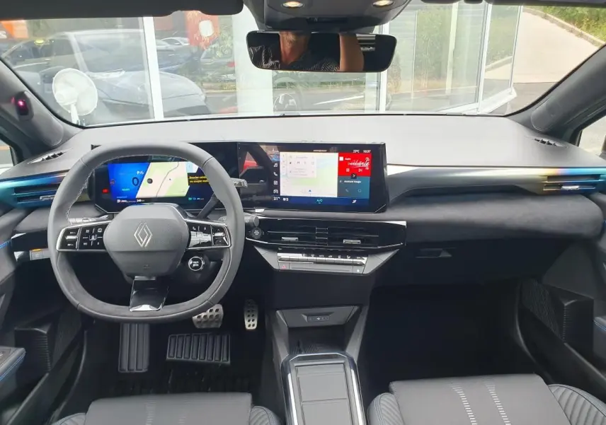Vue intérieure avant de la Renault Clio VI hybride, tableau de bord moderne avec écran tactile large et volant multifonction.