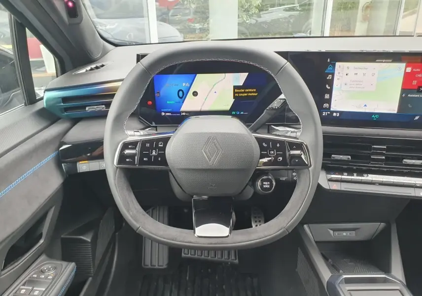 Vue frontale de l’habitacle de la Renault Clio VI hybride, volant multifonction et tableau de bord numérique.