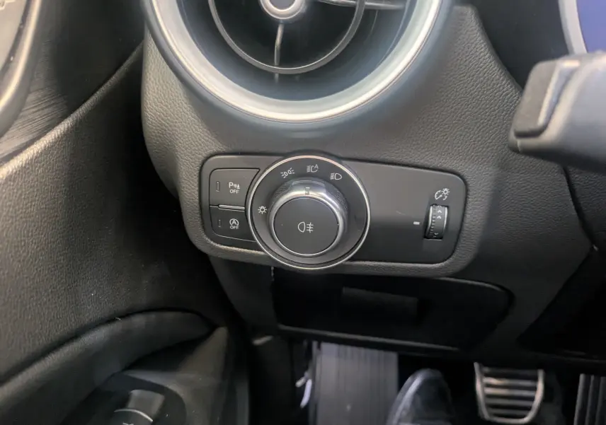 Gros plan sur le bouton de commande des phares et l'aération ronde du tableau de bord noir de l'Alfa Romeo Stelvio 2023.