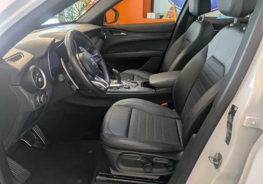 Intérieur côté conducteur d'un Alfa Romeo Stelvio blanc 2023, avec sièges cuir noir et tableau de bord moderne.