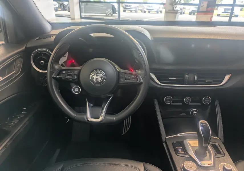 Intérieur noir de l'Alfa Romeo Stelvio 2023, vue frontale du poste de conduite avec volant et console centrale.