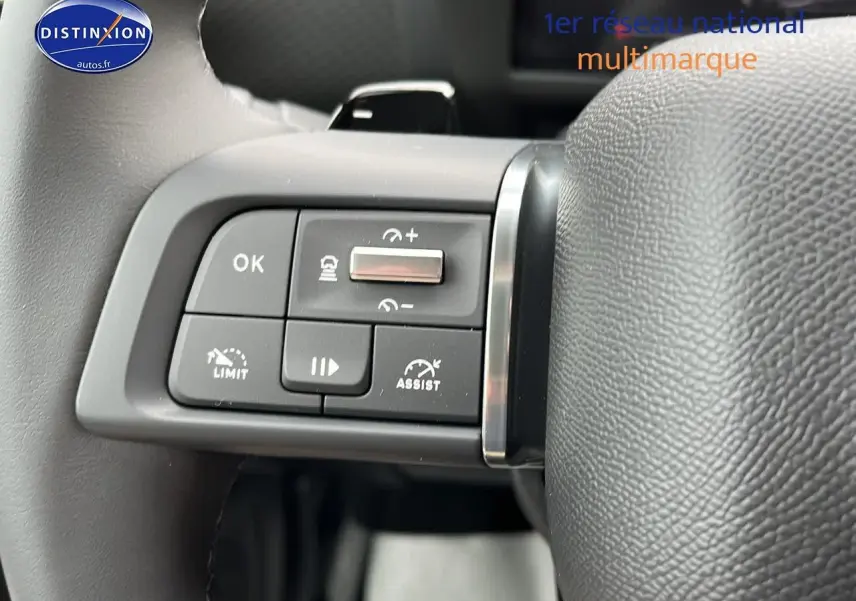 Gros plan sur les commandes au volant cuir noir d'une Citroën C4 noire métal 2025, côté gauche, avec régulateur adaptatif.