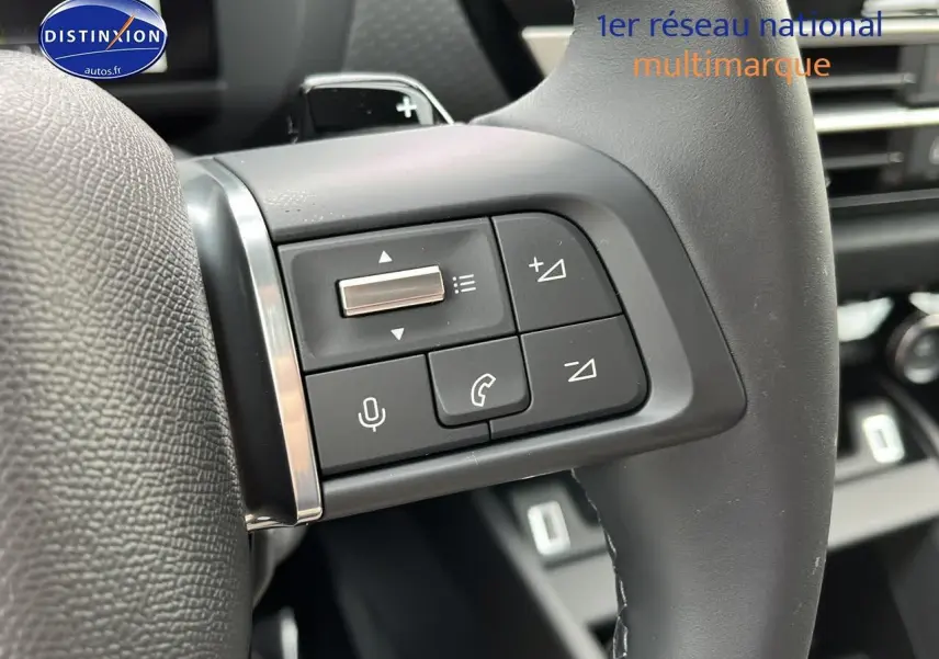 Gros plan sur les commandes gauche du volant cuir noir de la Citroën C4 1.2 hybride 2025, avec boutons multifonctions.