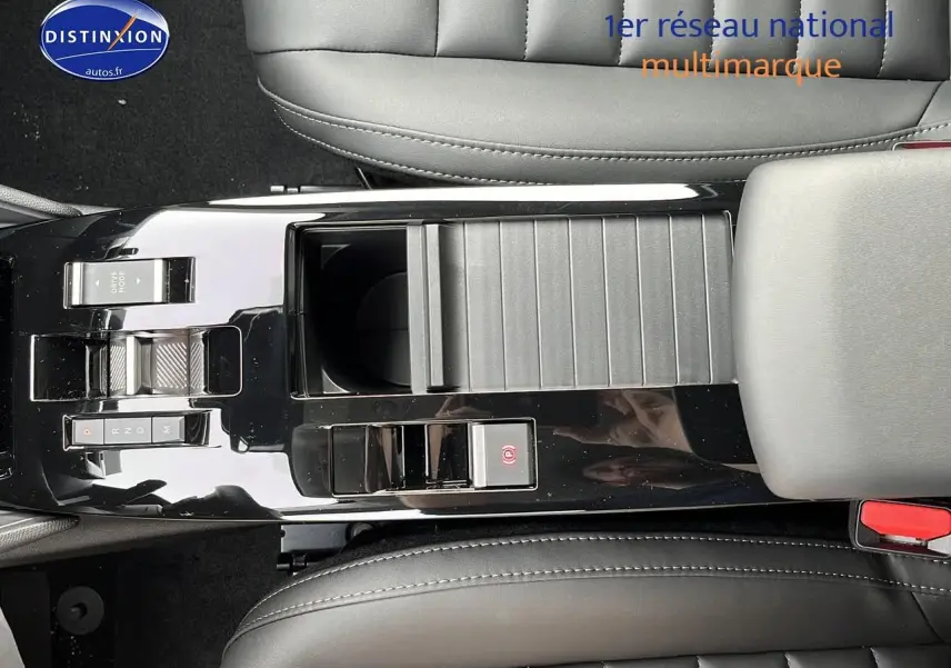 Vue plongeante sur la console centrale noire brillante du Citroën C4 1.2 hybride 2025 avec accoudoir et sièges cuir gris.