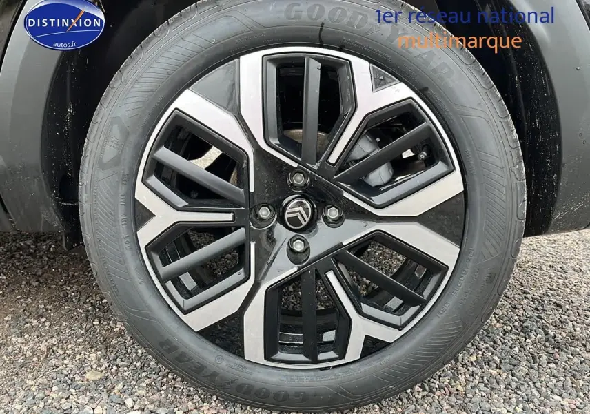 Vue latérale côté gauche d'une Citroën C4 noire métal avec jantes alliage 18 pouces sur sol gravillonné.