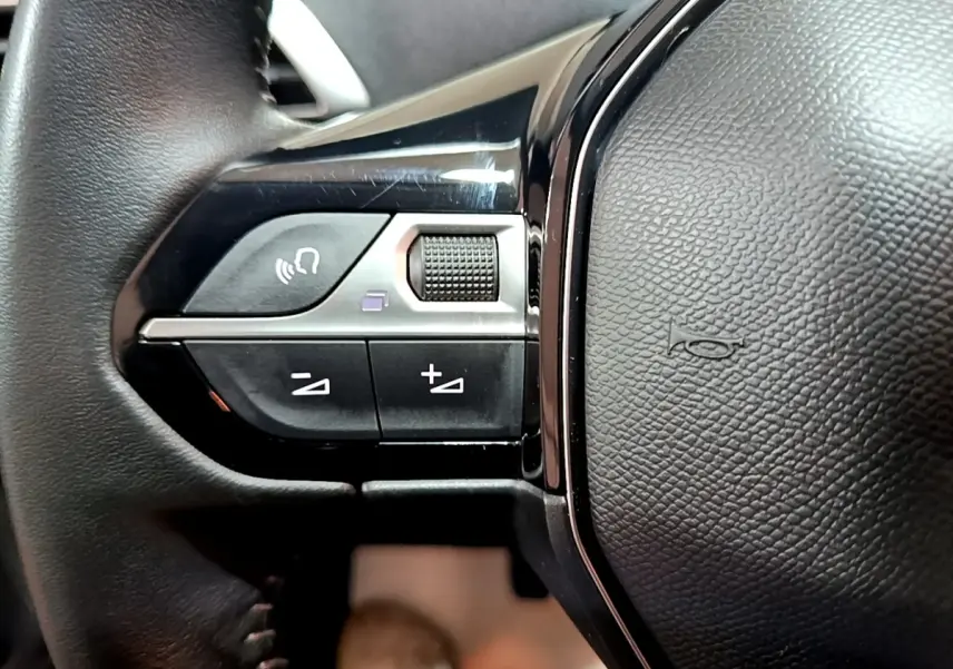 Gros plan sur les commandes gauche du volant cuir noir du Peugeot 3008 gris clair, avec boutons de volume et commande vocale.