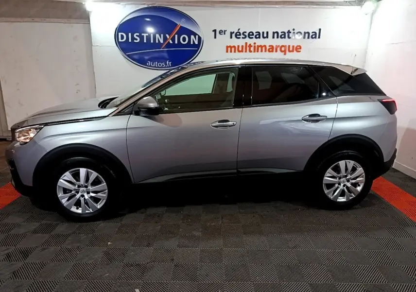 Vue latérale droite d'un Peugeot 3008 gris clair de 2020, avec jantes alliage et toit noir contrasté en intérieur showroom.
