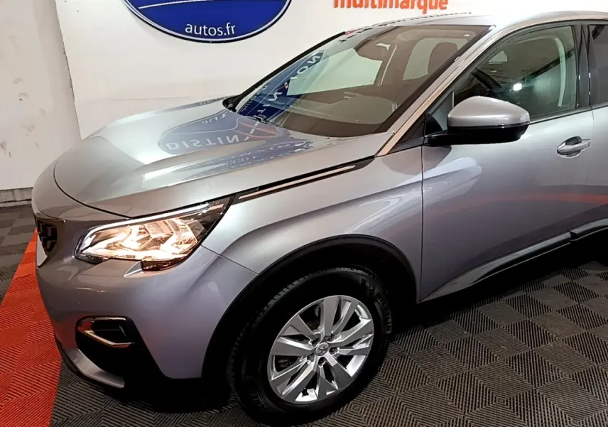 Vue 3/4 avant droit d’un Peugeot 3008 gris clair avec phares allumés et jantes alliage visibles.