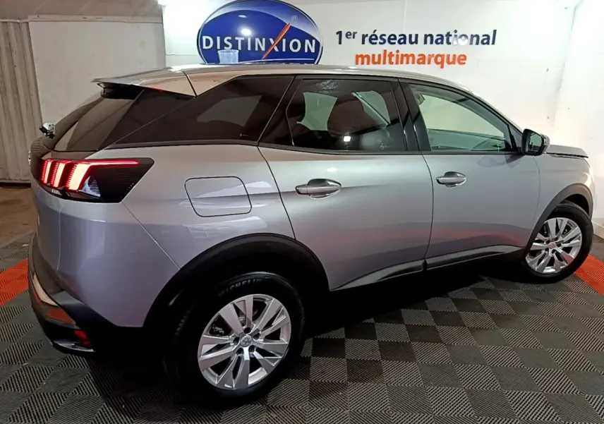 Vue 3/4 arrière droite d’un Peugeot 3008 gris clair avec feux LED distinctifs et jantes alliage en intérieur showroom.