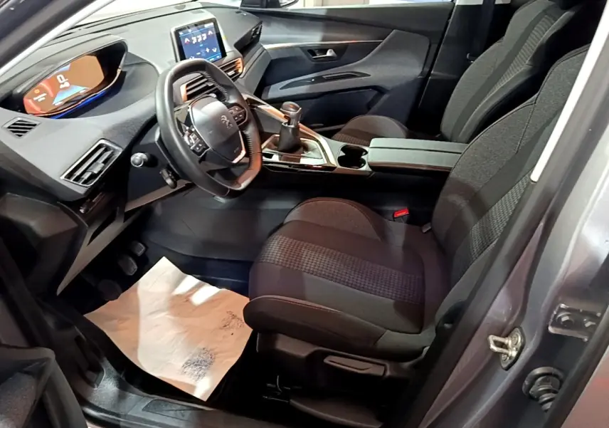 Vue intérieure côté conducteur du Peugeot 3008 gris clair, montrant le volant cuir, tableau de bord digital et levier de vitesse manuel.