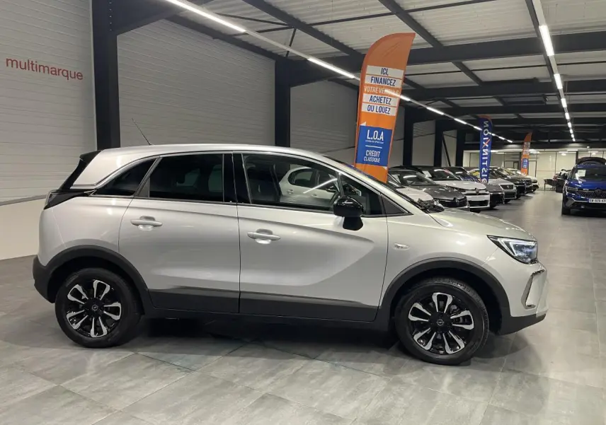 Vue de profil côté gauche d'un Opel Crossland gris clair avec jantes alliage diamantées en showroom.