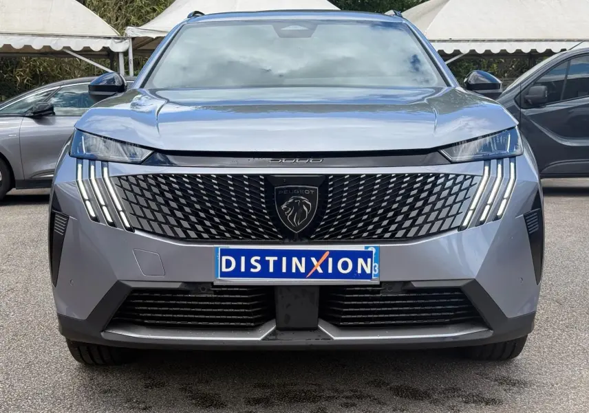 Vue frontale d'un Peugeot 5008 gris Artense 2025 avec calandre noire à motif géométrique et feux LED verticaux distinctifs.