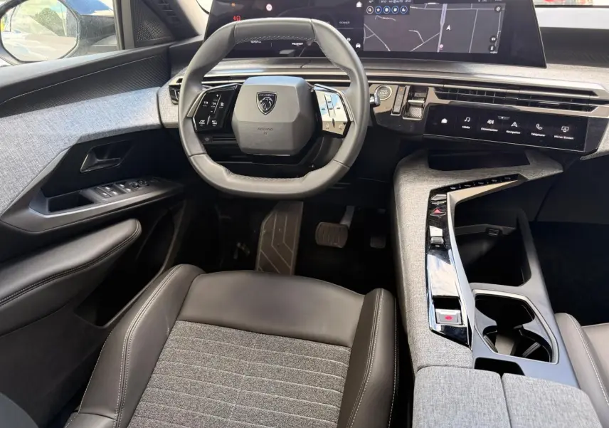 Vue intérieure avant du Peugeot 5008 Hybrid 145 en gris avec volant compact, tableau de bord numérique et console centrale en tissu gris.