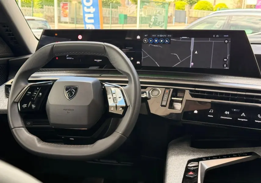 Vue intérieure centrée sur le volant compact et le tableau de bord numérique large du Peugeot 5008 Hybrid gris Artense.