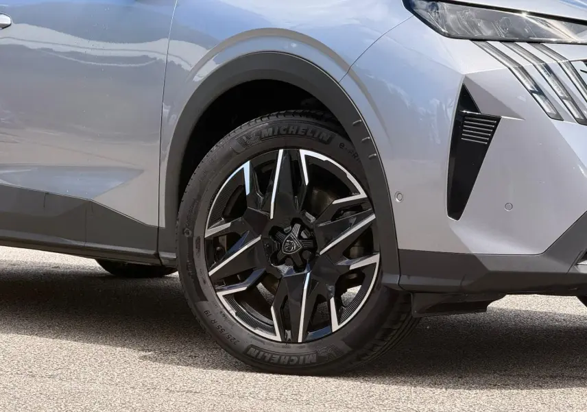 Gros plan sur la roue avant droite et partie avant d’un Peugeot 5008 gris Artense avec jante noire et argentée.