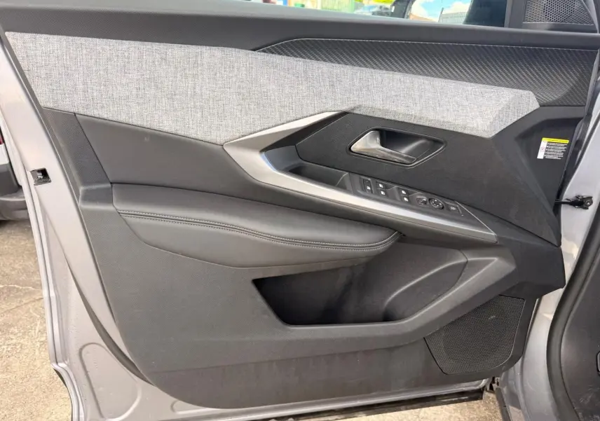 Vue intérieure côté gauche de la porte avant d’un Peugeot 5008 gris Artense, avec garniture tissu et commandes électriques.