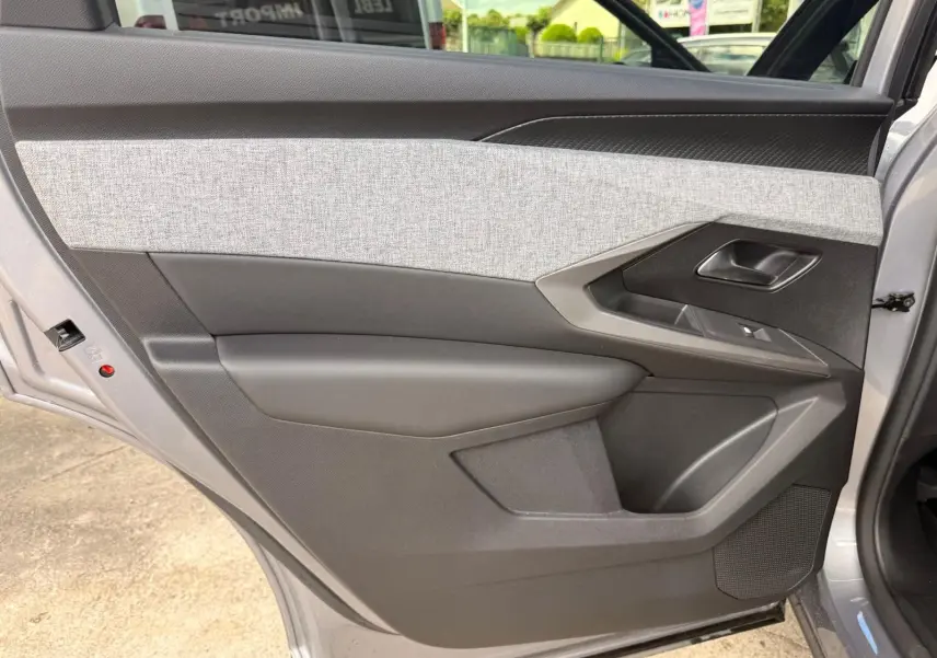 Vue intérieure du côté gauche de la porte arrière d’un Peugeot 5008 gris Artense, avec habillage tissu clair et plastique noir.